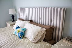 a bed with white and blue pillows on it's headboard next to a night stand