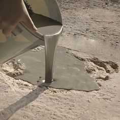 a person pouring cement into a bucket on top of a dirt ground with one hand