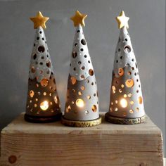 three ceramic christmas trees with gold stars on them, sitting on top of a wooden block