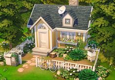 a small house with lots of flowers and plants in the front yard, next to a white picket fence