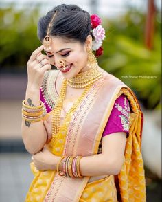 a woman in yellow and pink sari with jewelry on her neck, smiling at the camera