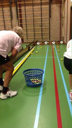 an image of two people playing table tennis on the same court as another person crouches down to pick up some balls