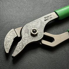 a green handled pliers sitting on top of a black leather covered table next to a pair of scissors