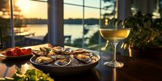 a plate of oysters next to a glass of wine on a table near a window