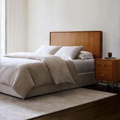 a bed with white sheets and pillows on top of it next to a wooden dresser