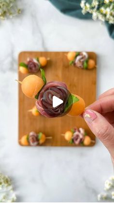 a person is holding an orange and beet skewer on a wooden board