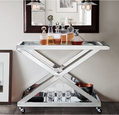 a bar cart with liquor bottles and glasses on it in front of a framed mirror