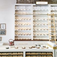 a room with shelves filled with jars and candles next to a ladder in the wall