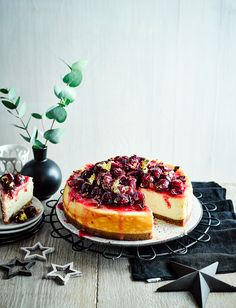 a cheesecake with cranberry toppings on a plate next to a vase