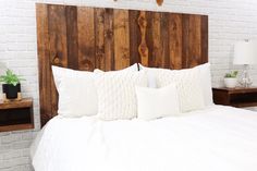 a bed with white pillows and wooden headboard against a brick wall in a bedroom