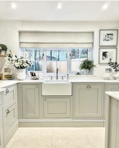 a white kitchen with gray cabinets and pictures on the wall above the sink, along with potted plants