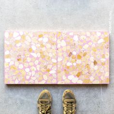 a pair of shoes sitting on top of a floor next to a wall covered in pink and gold pebbles