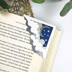 an open book sitting on top of a table next to a plant and some leaves