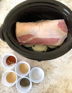 the ingredients are in small bowls next to an open crock pot with raw meat