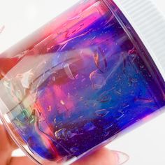 a hand holding a jar filled with blue and pink liquid on top of a white surface