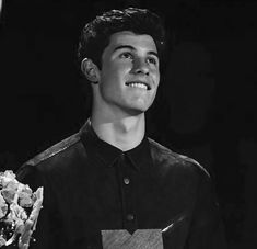 the young man is holding flowers in his hand and smiling at the camera as he stands on stage