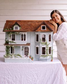 a woman standing next to a doll house