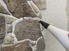 someone is using a sharpie to paint a stone wall with white and gray colors