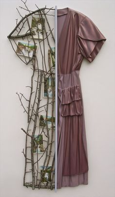 a dress hanging on a wall next to a tree branch with pictures in the back