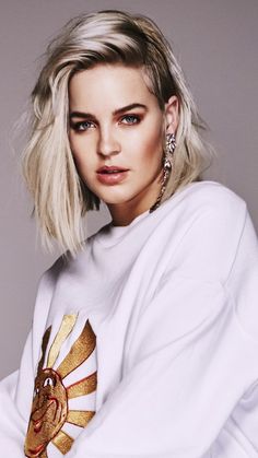 a woman with blonde hair wearing a white shirt and gold earrings, posing for a photo