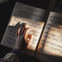 someone is writing on sheet music with their hand in the light from an open book