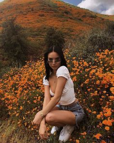 a woman is sitting on the ground in front of some wildflowers with her legs crossed