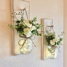 two mason jars with flowers are hanging on the wall