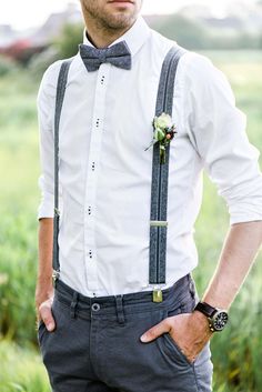 a man wearing suspenders and a bow tie is standing in the grass with his hands on his hips