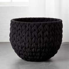 a large black basket sitting on top of a cement floor in front of a window