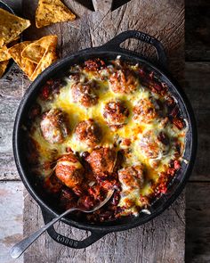 a skillet filled with meatballs and cheese next to tortilla chips on a wooden table