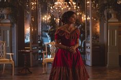 a woman in a red dress standing in a room with chandeliers