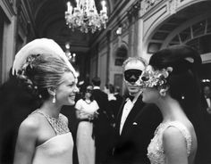 black and white photograph of two women in formal wear talking to each other while people look on