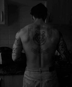 a man with tattoos on his back standing in a kitchen