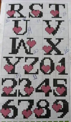 a cross - stitch pattern with hearts and letters in the middle, on top of a piece of paper