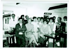 a group of people standing around each other in front of a desk with computers on it