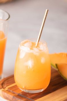 two glasses filled with orange juice on top of a wooden tray next to sliced watermelon