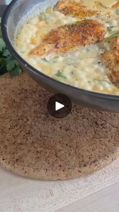 a pan filled with chicken and cheese on top of a cork place mat next to a pot holder