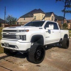 a white truck parked in front of a house with large tires on it's tires