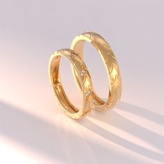 two gold wedding rings sitting side by side on a white surface with the light shining through them