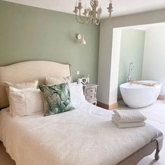 a bedroom with a large bed, chandelier and bathtub in the background