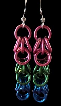 two pairs of colorful earrings hanging from hooks on a black background with the same color