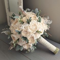 a bridal bouquet with white flowers and greenery on a wooden table in front of a mirror