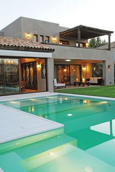 a large swimming pool in front of a house with an open patio and lawn area