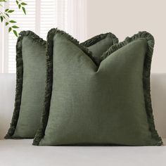 two green pillows sitting on top of a white couch next to a potted plant