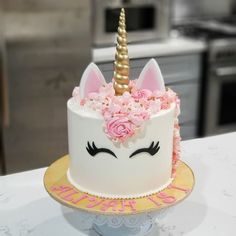 a white cake decorated with pink flowers and a unicorn's face