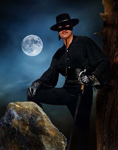 a man in a black outfit and hat sitting on a rock next to a tree