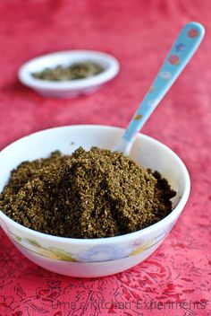 a bowl filled with green powder next to two spoons on a red tablecloth