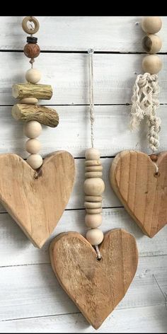 three wooden hearts hanging from strings on a white wood planks wall with beads and chains