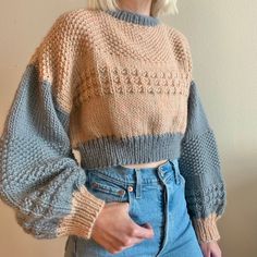 a woman with blonde hair wearing blue jeans and a knitted sweater stands in front of a wall