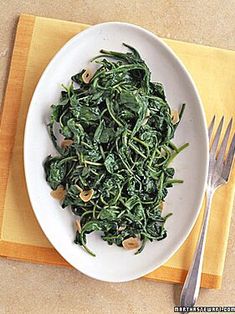 a white plate topped with spinach and nuts next to a fork on a yellow place mat